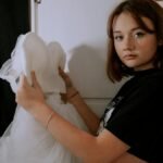 Teen girl holding a wedding dress indoors, conveying contemplation and future planning.