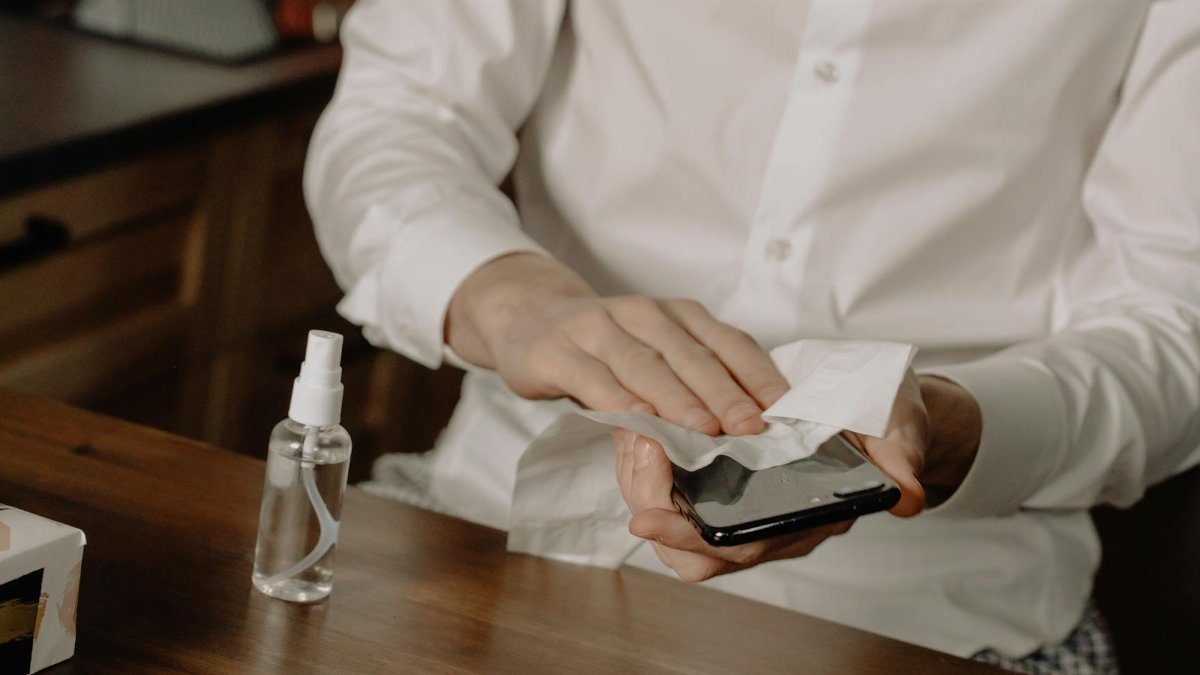 A person sanitizes their smartphone at a table, promoting healthy hygiene in home settings.