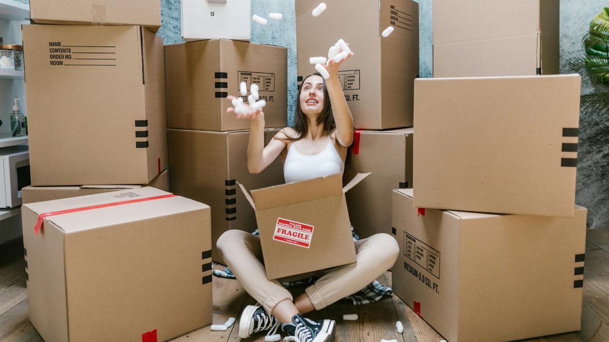 Young woman surrounded by cardboard boxes, happily moving into her new apartment.