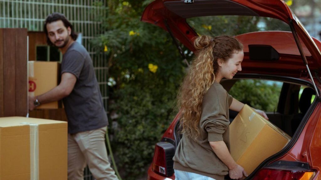 A cheerful young couple unloading boxes from a car trunk into their new home in the countryside.