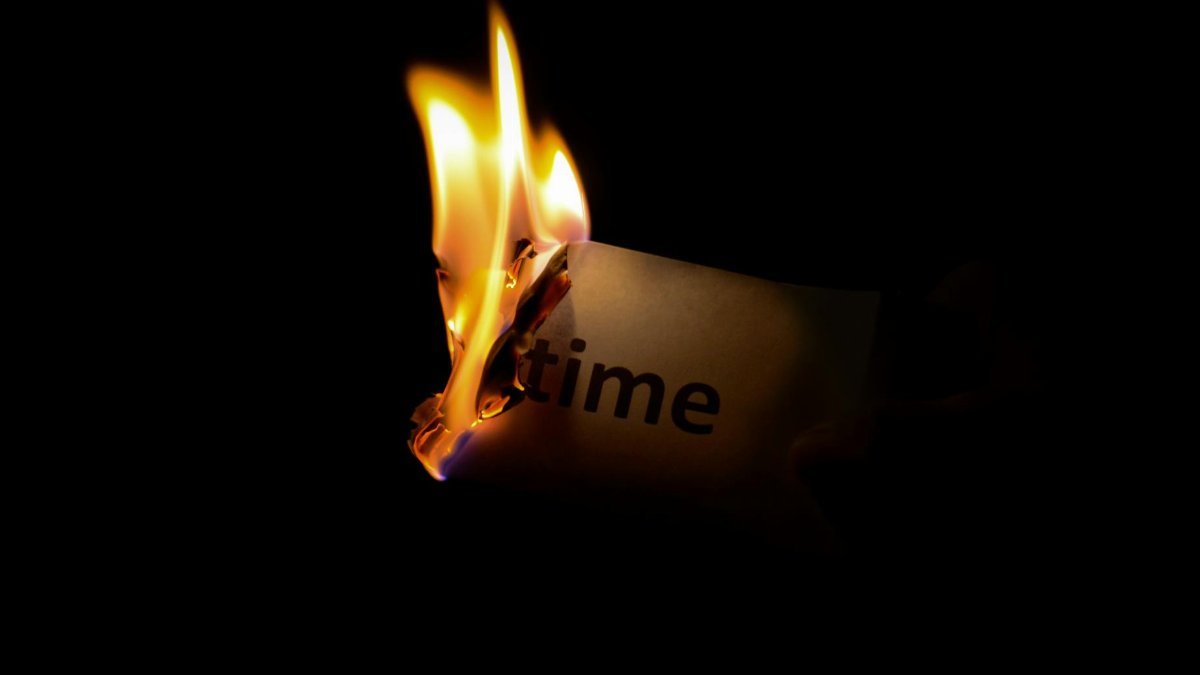A close-up of a paper with the word 'time' burning against a dark background.