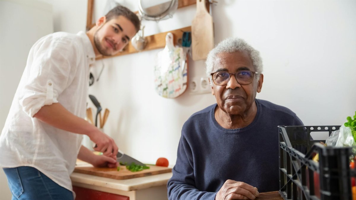 A young adult helping a senior in the kitchen, highlighting care and support at home.