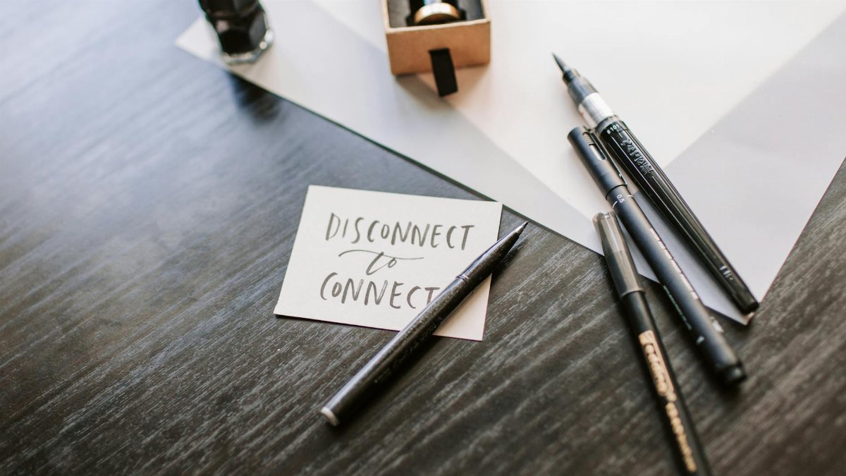 A motivational 'Disconnect to Connect' note surrounded by pens and ink on a wooden desk.