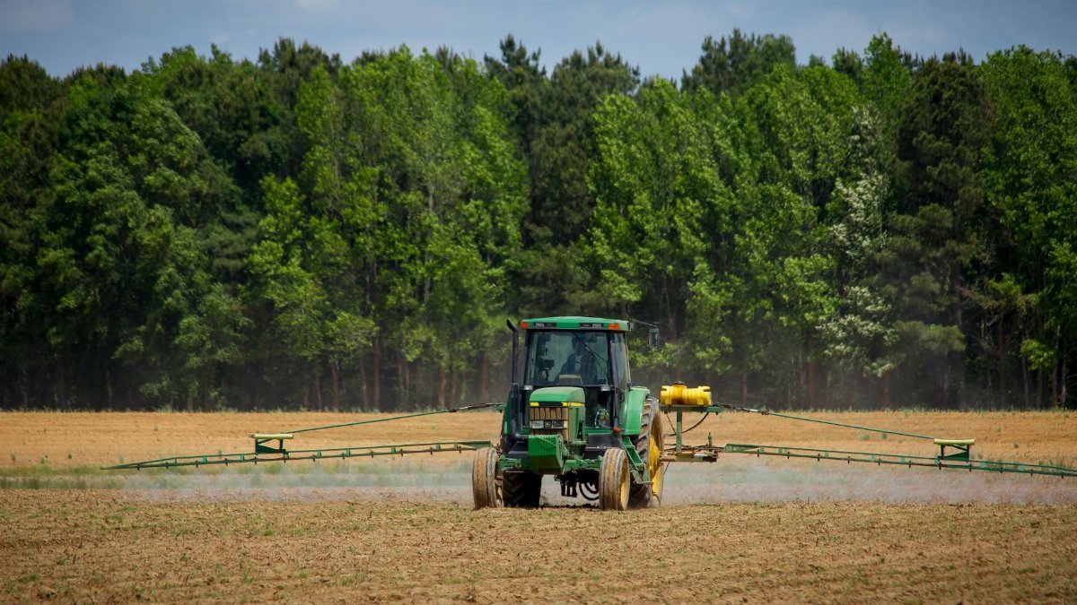 Tractor spraying fields with pesticides on a countryside farm in summer with a forest backdrop.