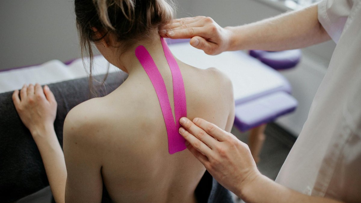 A healthcare professional applies kinesiology tape on a woman's neck for therapeutic treatment.