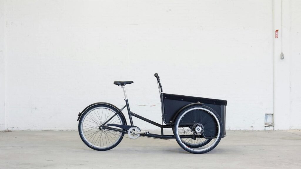 Side view of a three-wheeled cargo bike in a minimalistic indoor setting.