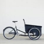 Side view of a three-wheeled cargo bike in a minimalistic indoor setting.