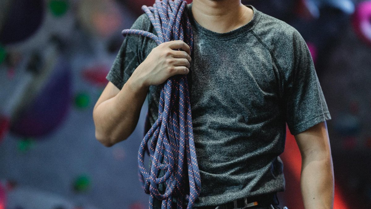Crop unrecognizable male athlete in sportswear with belay and rope standing in bouldering center