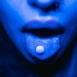Dramatic close-up of a person with a tablet on their tongue in blue lighting.