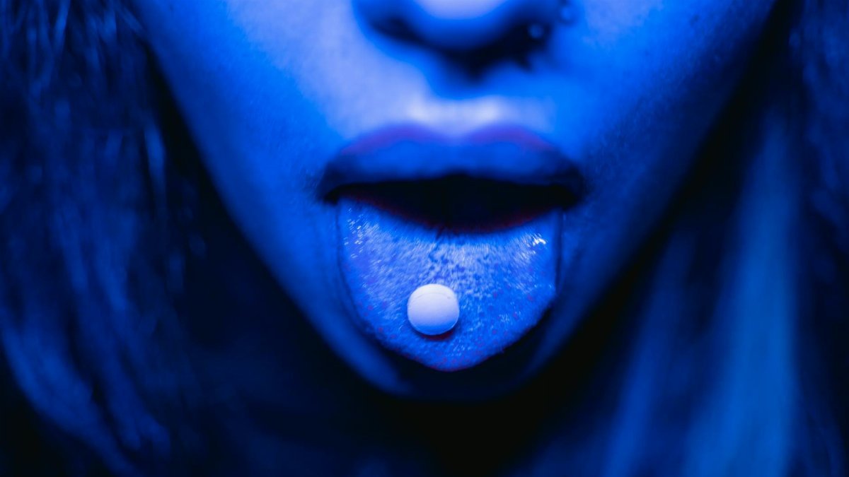 Dramatic close-up of a person with a tablet on their tongue in blue lighting.