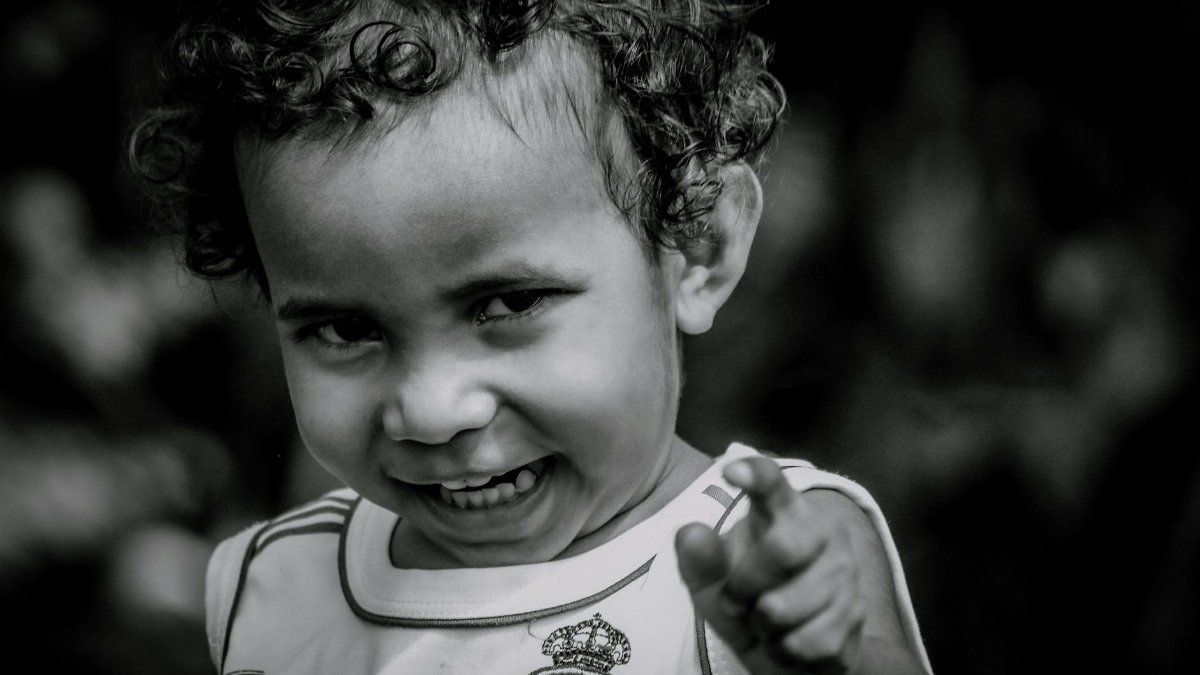Smiling child pointing playfully, in monochrome, outdoors in Agats, Indonesia.