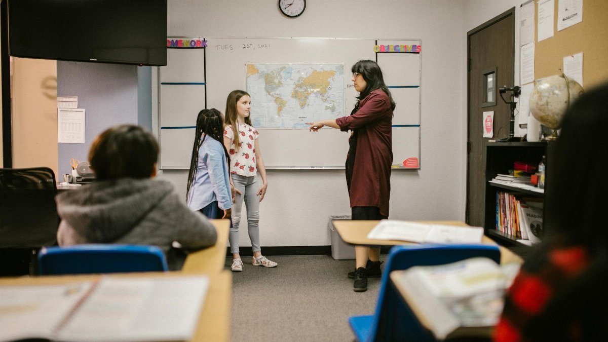 A teacher instructs students in a classroom with a world map and educational materials.