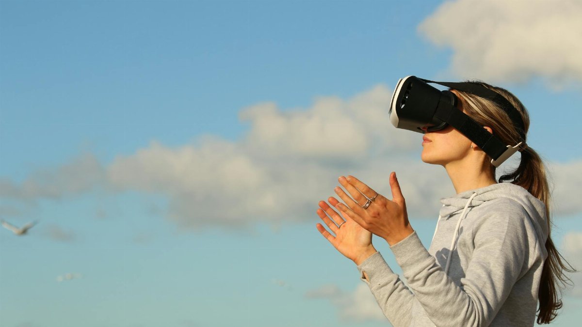 Woman using VR headset outdoors, exploring virtual reality under a clear blue sky.