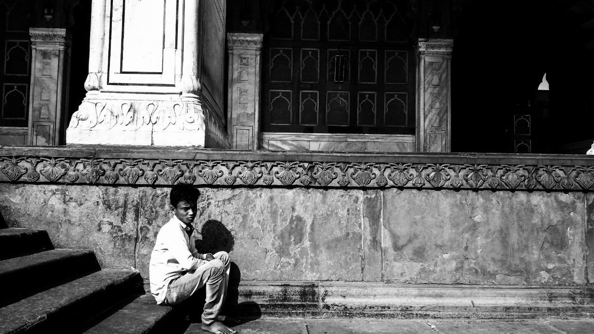 A young boy sitting on historic steps in Delhi, conveying solitude and contemplation.