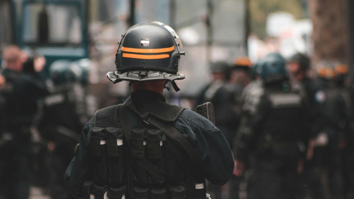 Back view of anonymous policeman in helmet and bulletproof vest maintaining law and order while standing on city street