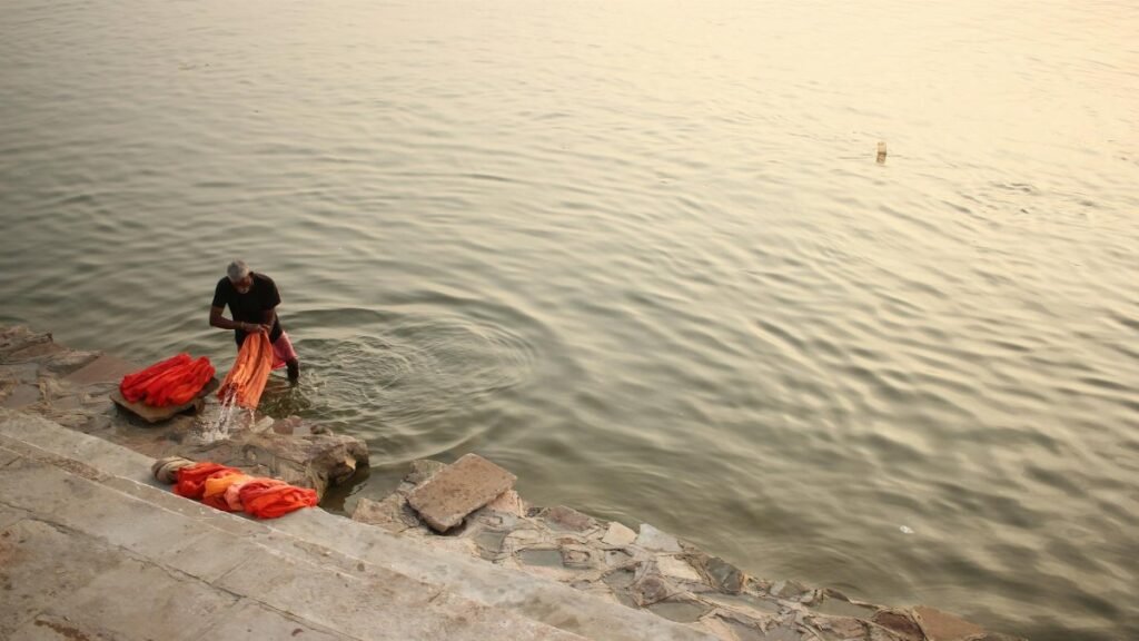 A man washing clothes by the river in Varanasi at sunset, showcasing traditional lifestyle.