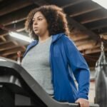 Low angle of plump African American female standing on treadmill in gym and looking away