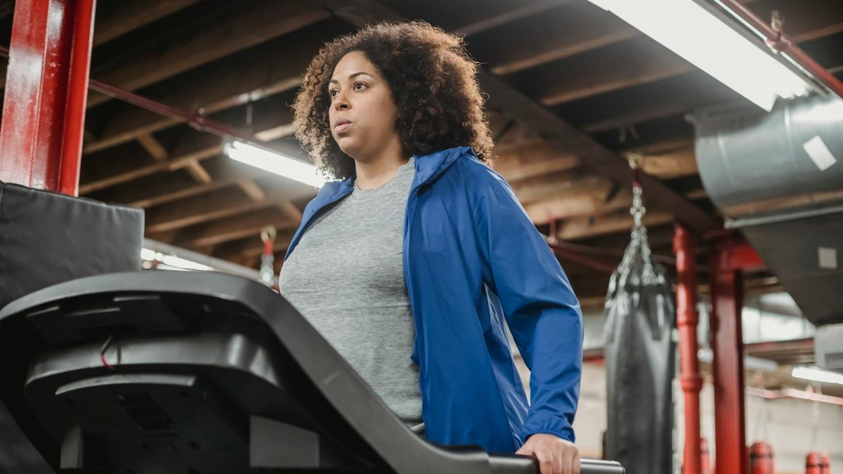 Low angle of plump African American female standing on treadmill in gym and looking away