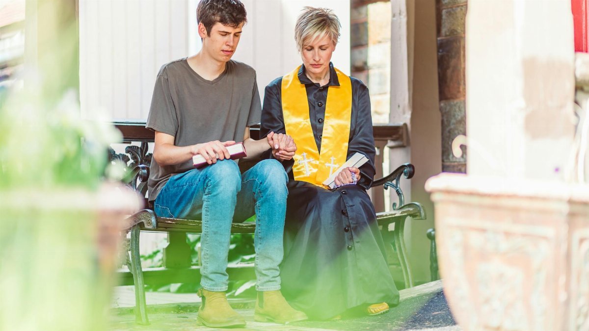A clergy member and a young adult praying together outdoors, offering comfort and support.