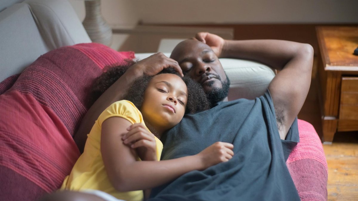 A peaceful moment with father and daughter asleep together on the couch, capturing family bond.