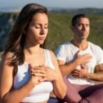 Two adults meditating outdoors in Portugal, embracing a serene yoga practice under the sun.