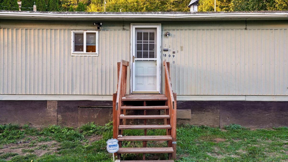Exterior view of a mobile home with wooden steps on a sunny day.
