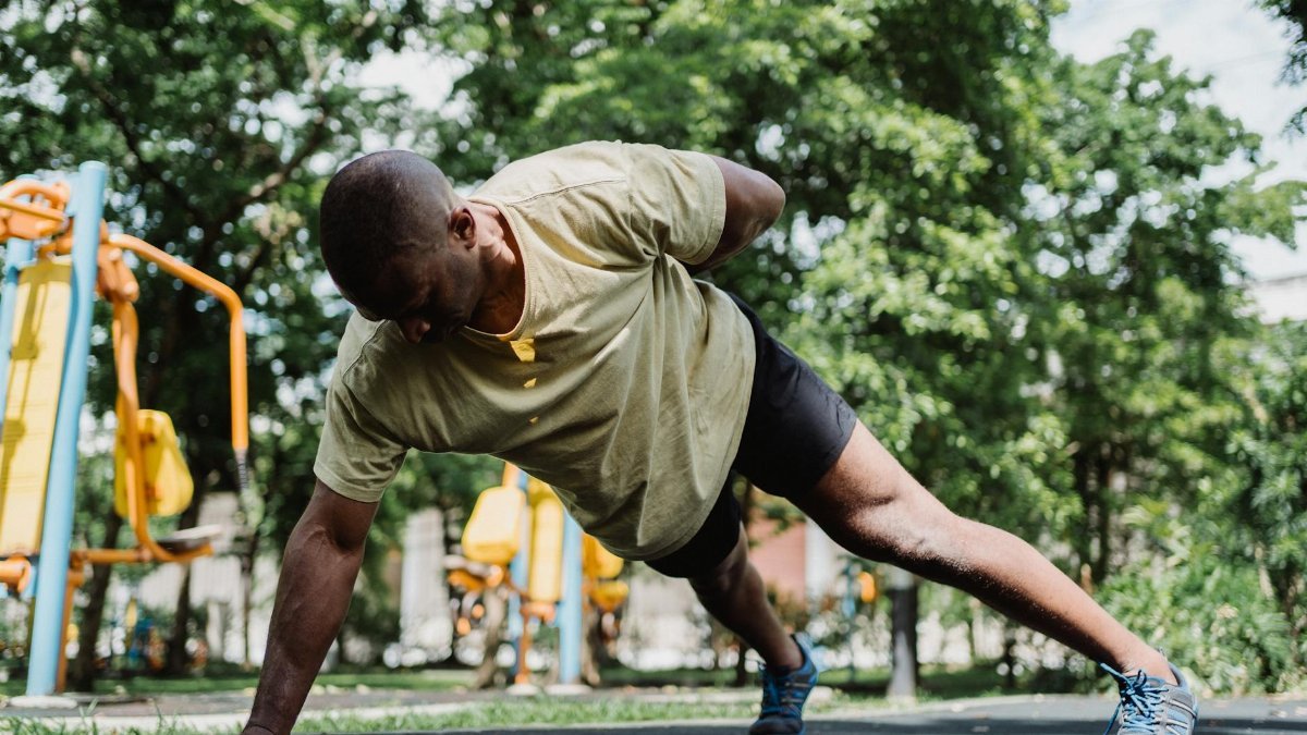 Fit man doing a one-arm push-up outdoors in a park setting, emphasizing strength and endurance.