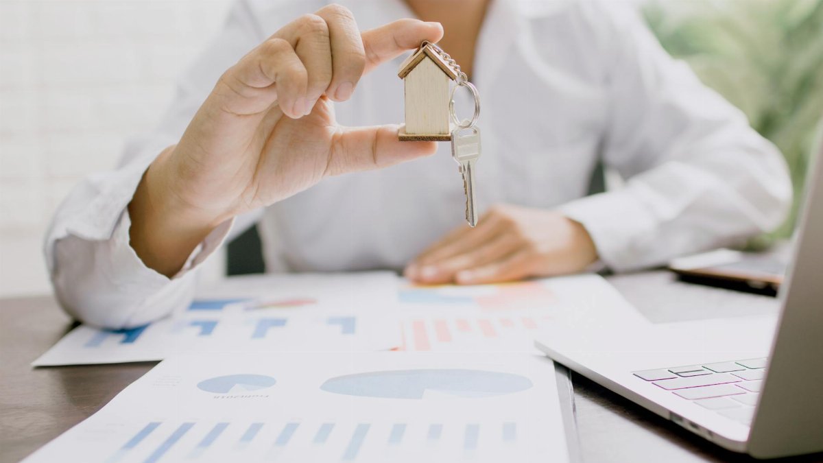 Real estate professional presenting a house model with keys, symbolizing property investment and ownership.