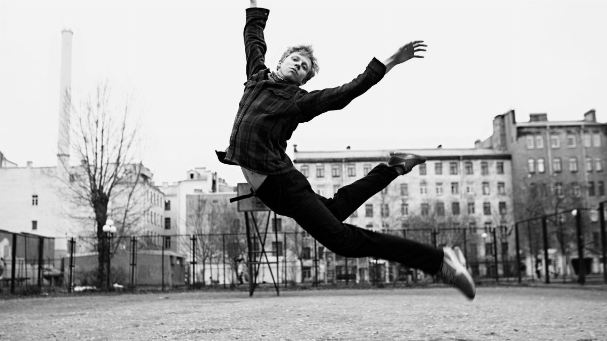 A dancer gracefully leaps mid-air in a black and white urban landscape.