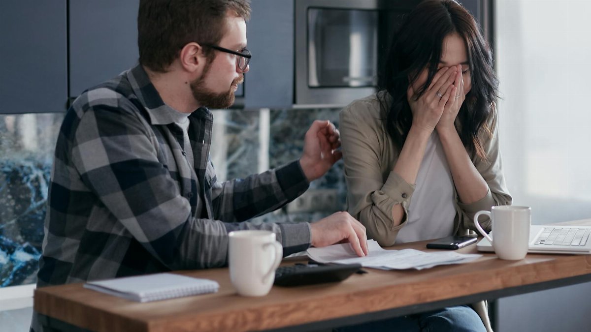 A couple discusses financial issues with bills and a laptop on the table, inside a modern kitchen setting.