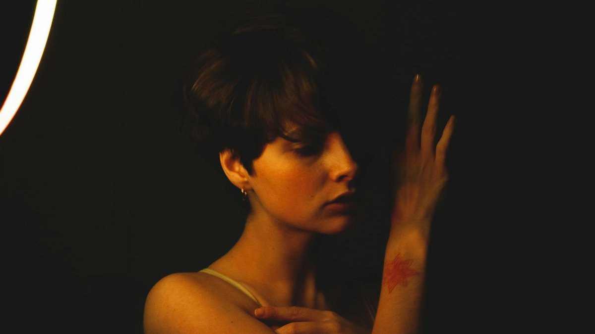 Artistic portrait of woman with short hair and tattoo, moody lighting, side view.