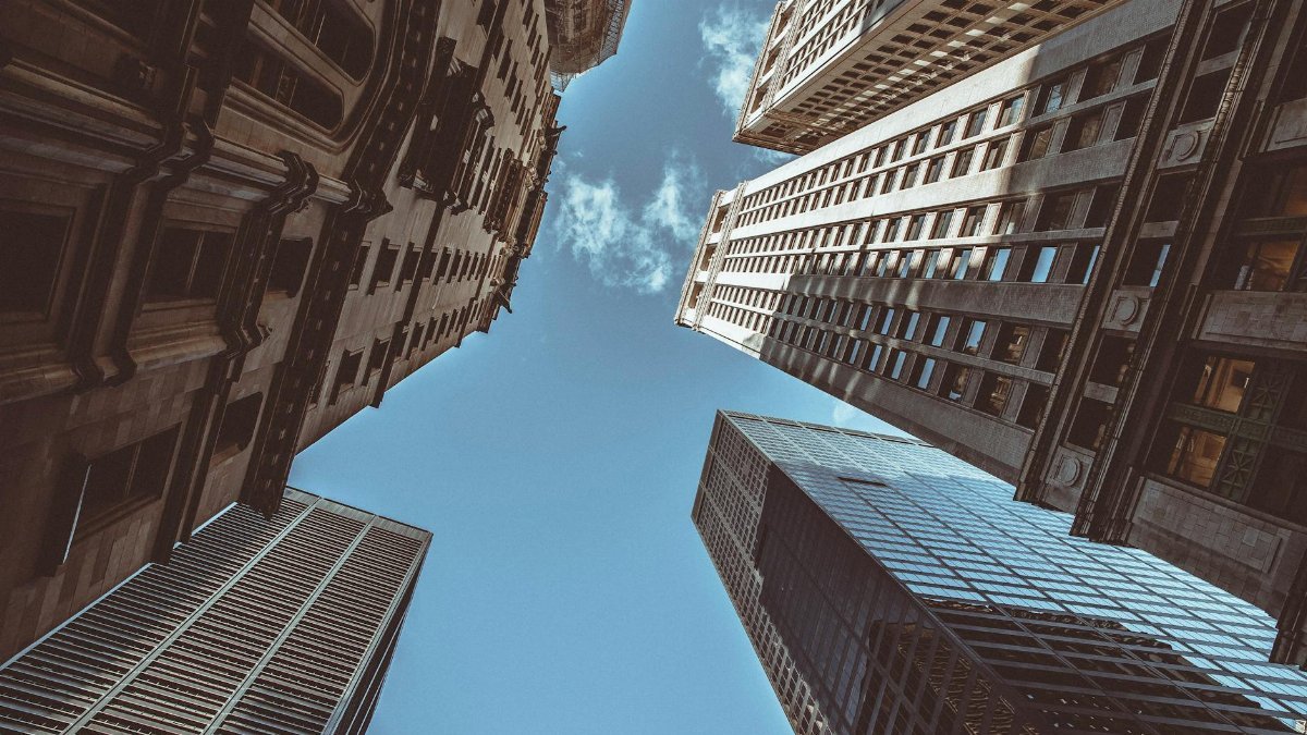 Upward perspective of New York skyscrapers against a clear blue sky, showcasing urban architecture.