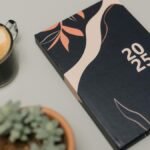 A modern 2025 planner next to a cup of coffee and a potted succulent on a neutral background.