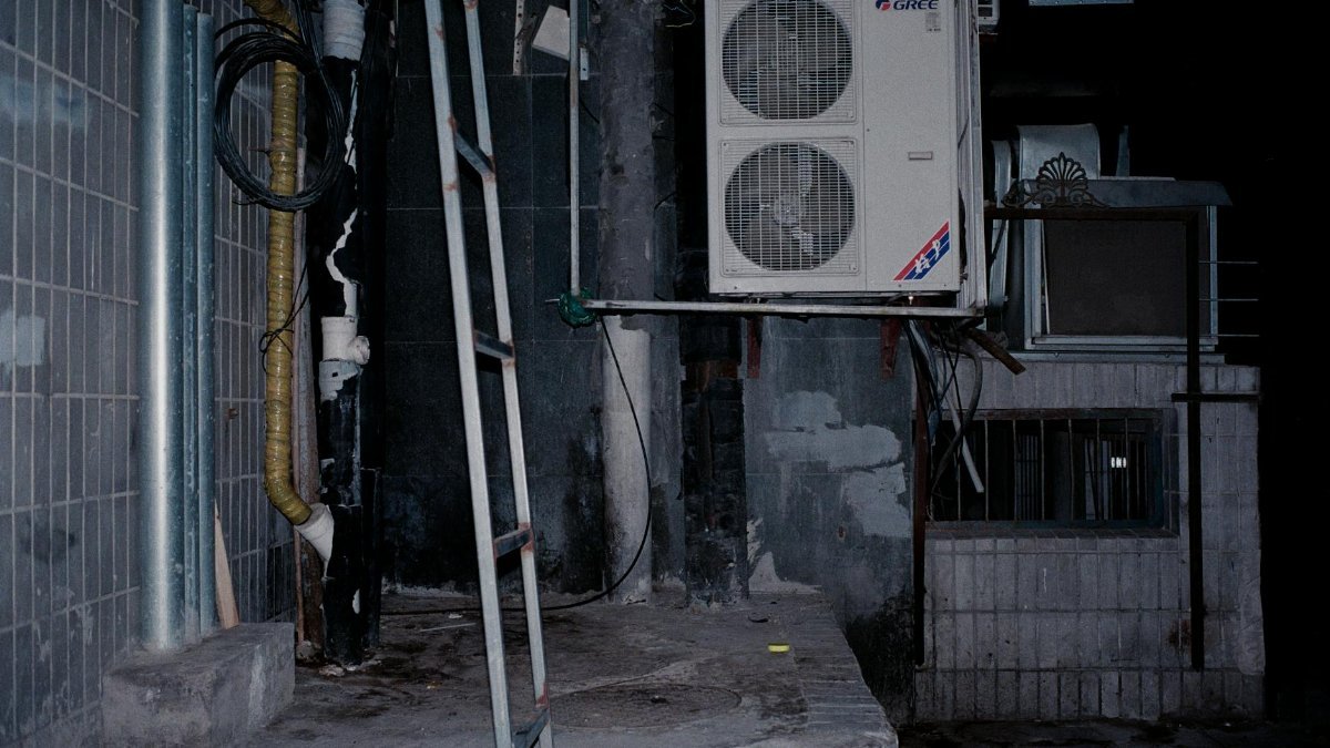 Close-up of an industrial air conditioner setup on a building wall, showcasing pipes and a ladder.