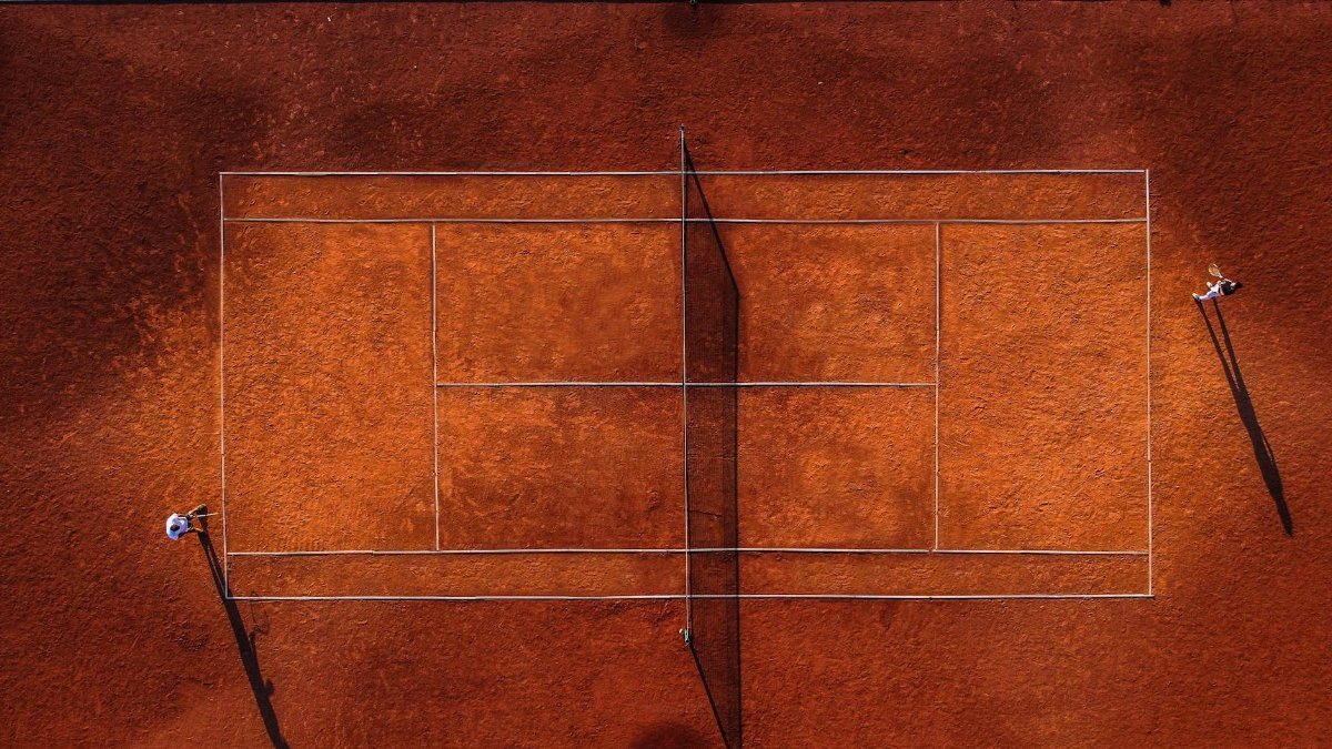 Drone shot of a tennis match on a clay court with players in action.