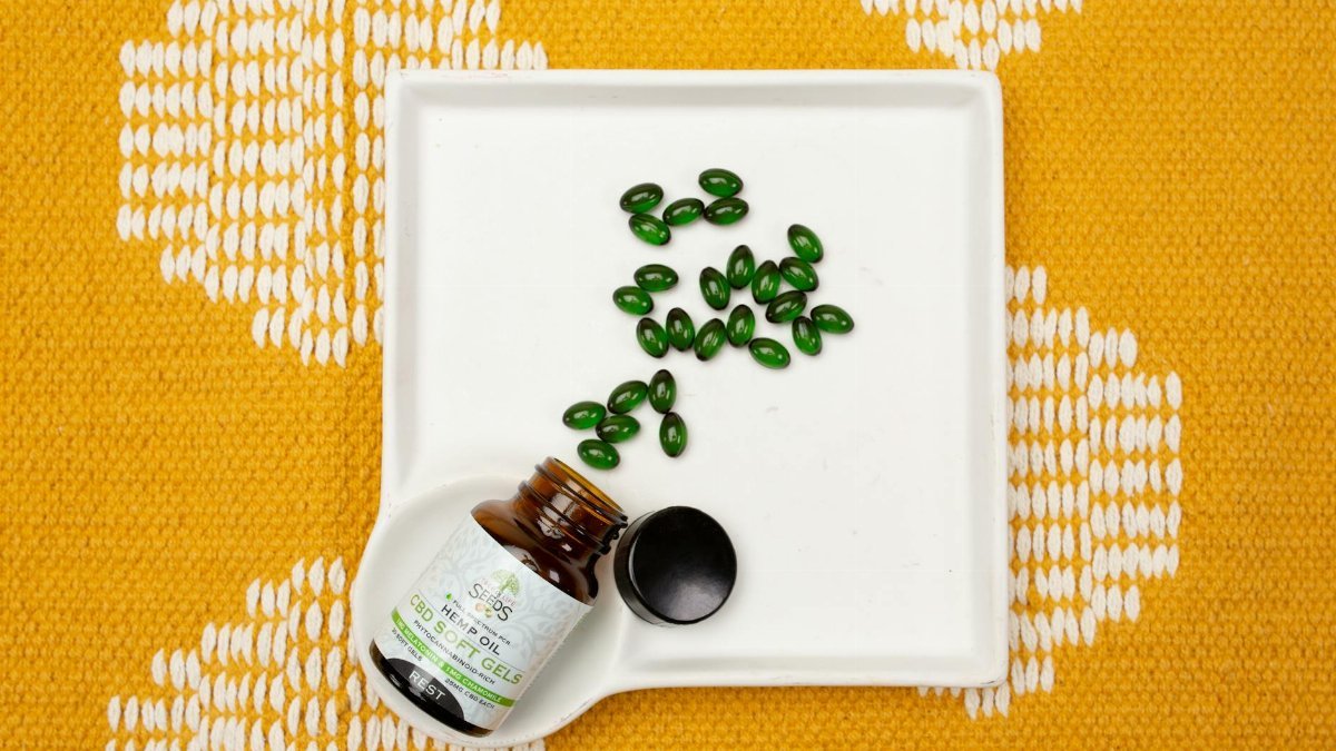CBD oil capsules in a bottle on a white tray over an orange patterned fabric. Ideal for health and wellness themes.