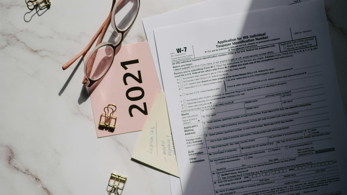 Flat lay of IRS tax documents with reading glasses and 2021 note on a marble surface.
