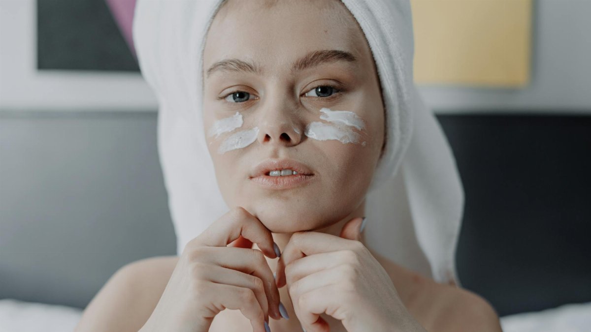 Portrait of a young woman with facial cream, wrapped in a towel, indoor setting.