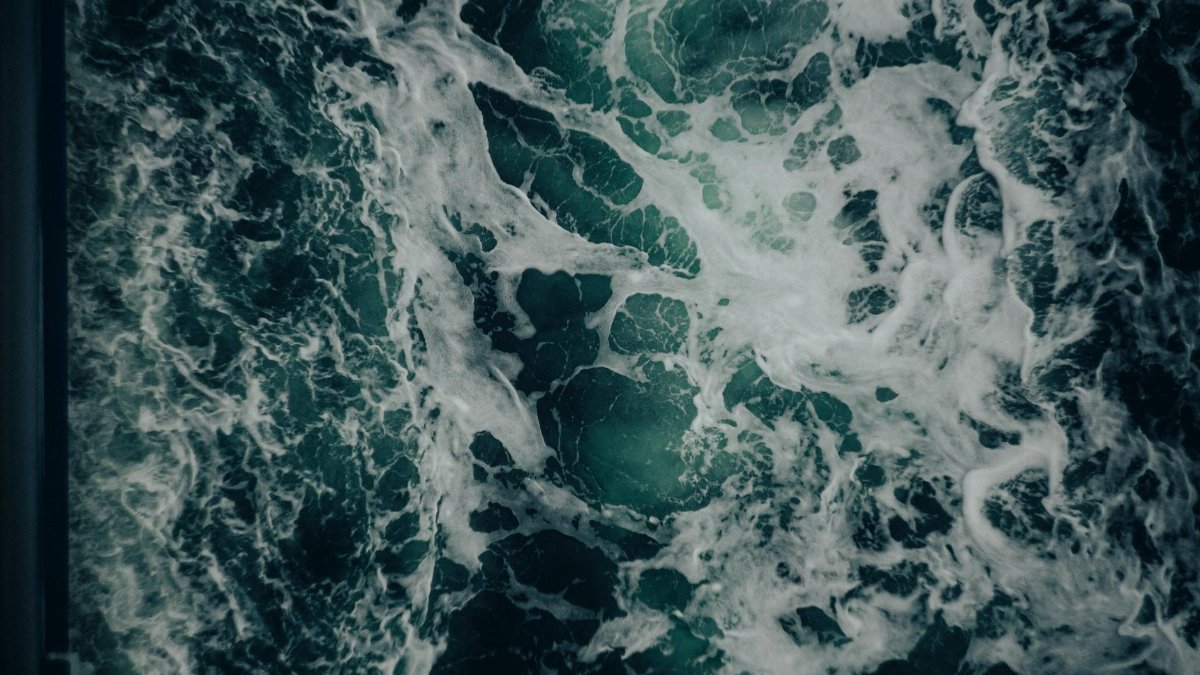 Dynamic aerial capture of ocean waves creating frothy patterns.
