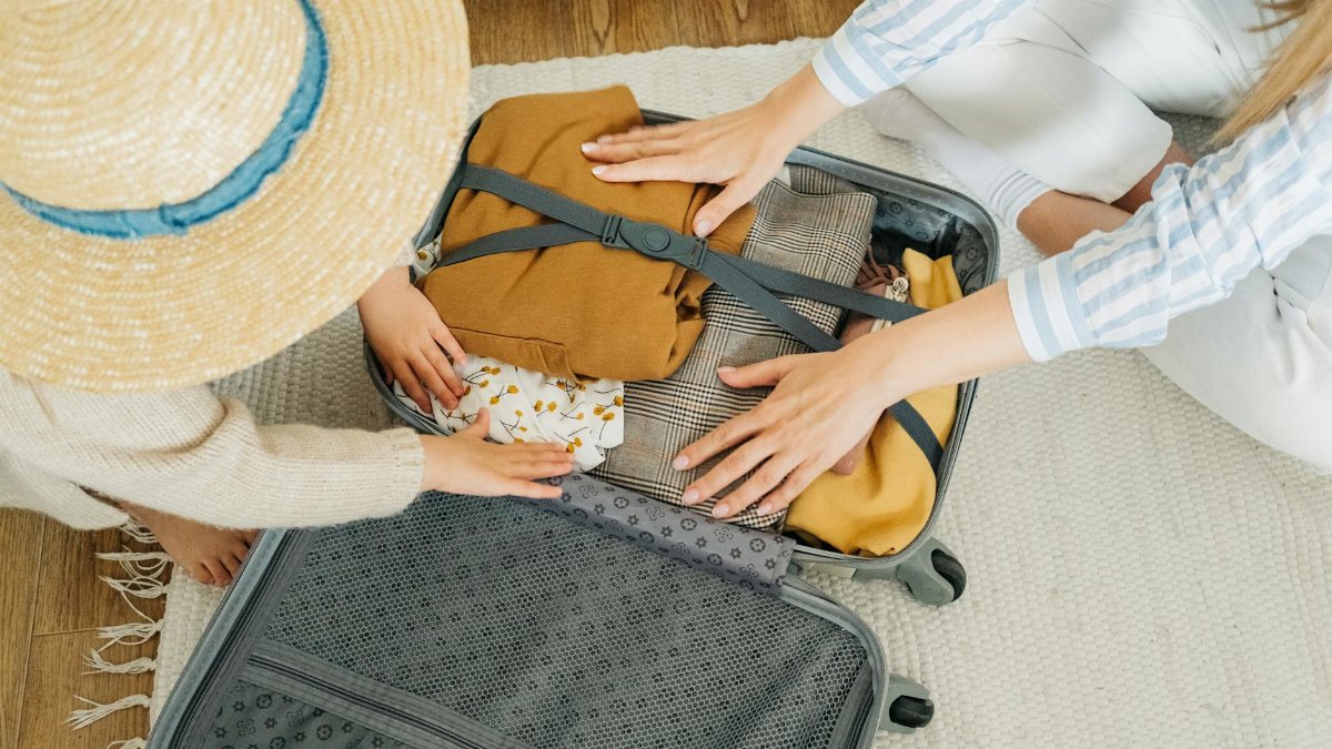 A woman and child pack clothes in a suitcase, preparing for a vacation.
