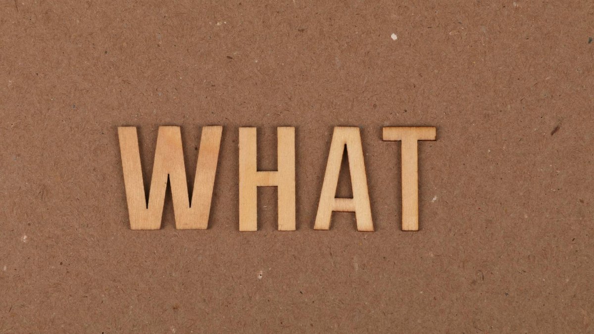 Wooden letters spelling 'What' on a brown cardboard background, close-up view.
