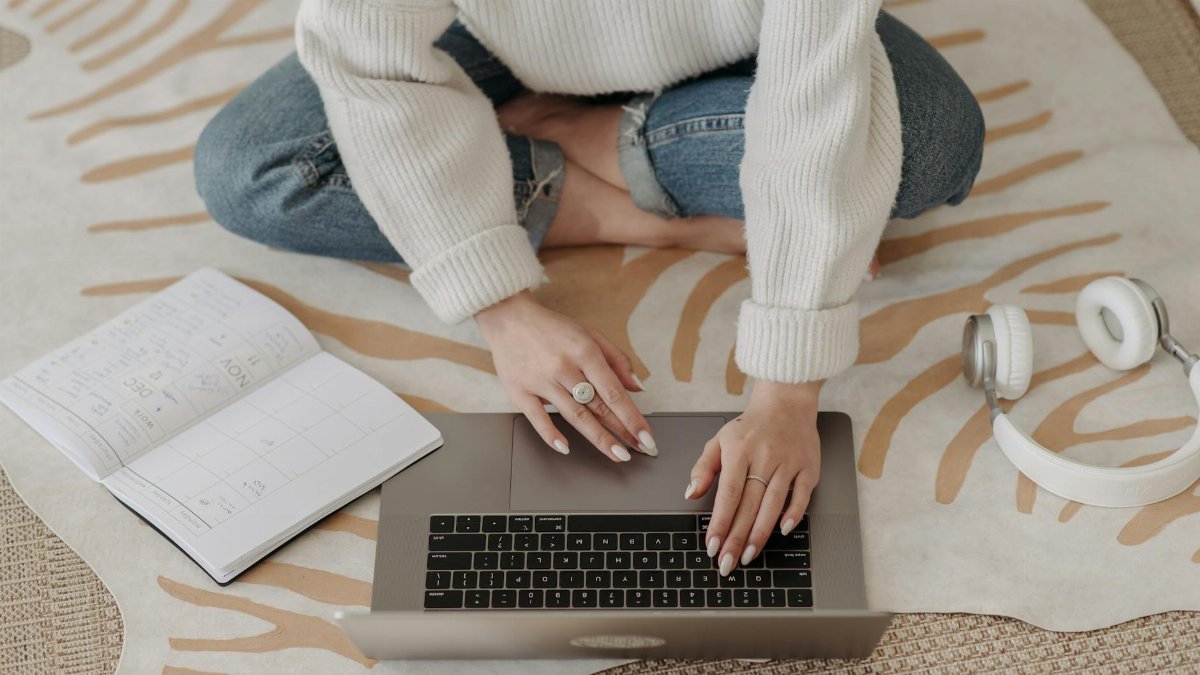 Person typing on a laptop with planner and headphones, showcasing a cozy home workspace.
