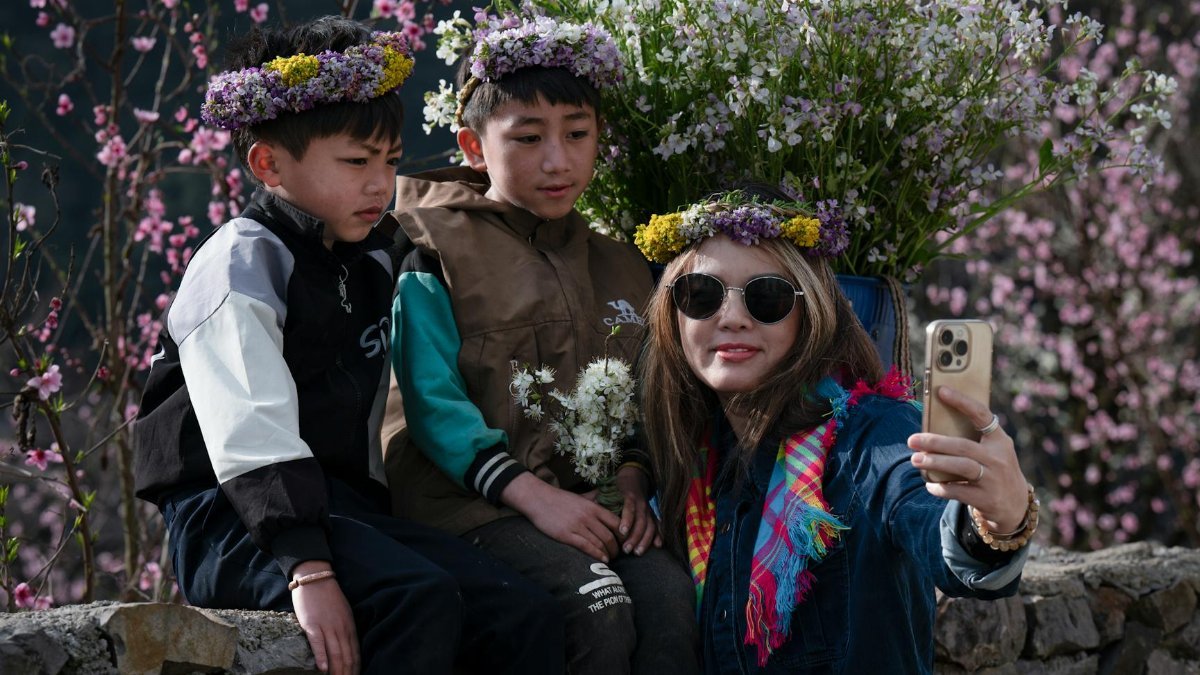 Family taking a selfie with flower crowns in a blooming garden. Capturing springtime joy and nature's beauty.