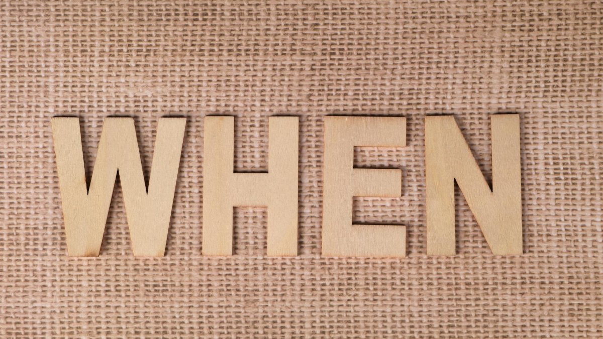 Wooden letters spelling "WHEN" on a textured burlap surface, ideal for concepts of time and planning.
