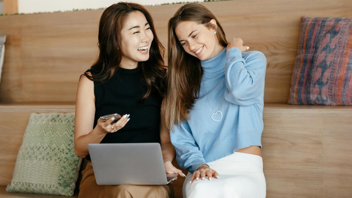 Cheerful young multiracial friends smiling and surfing internet on netbook while using mobile phone