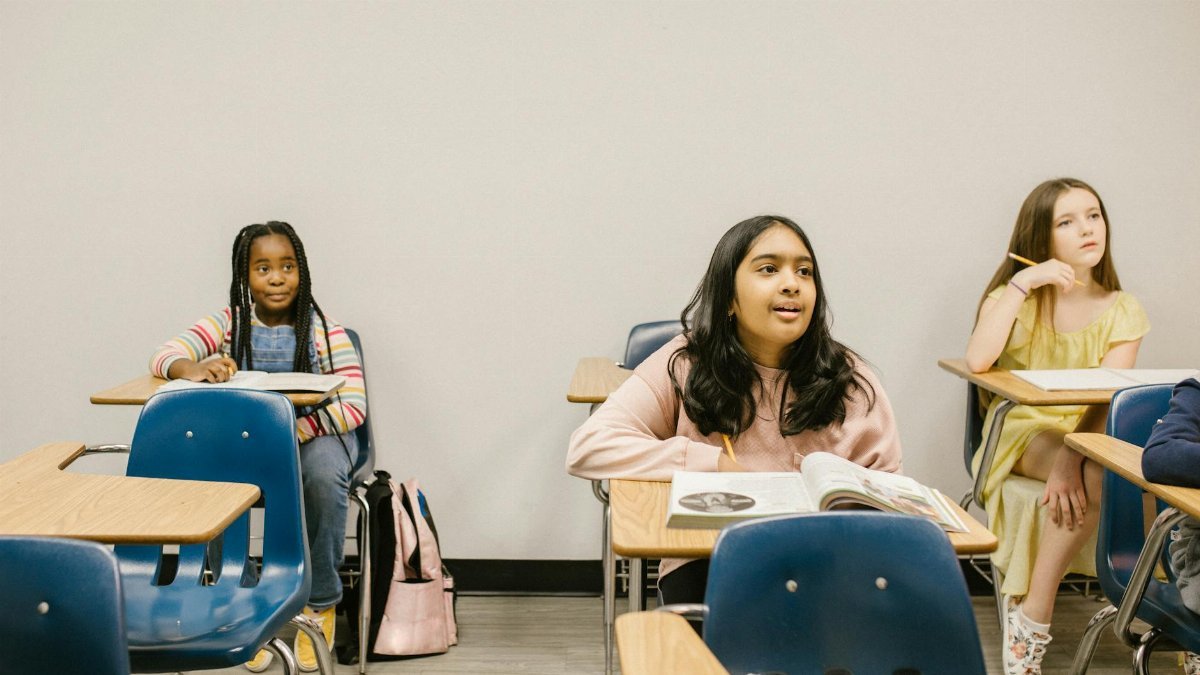 Three diverse students sitting in a classroom, engaged in learning.