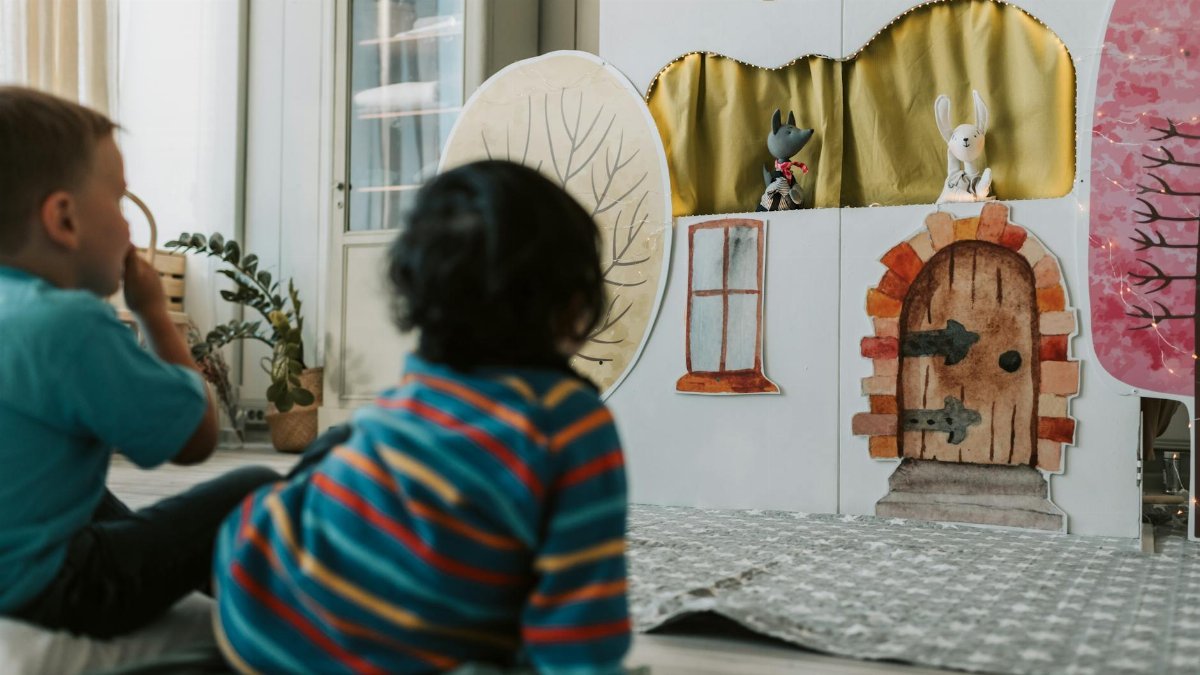 Kids engaged in a puppet theater, watching with fascination indoors.