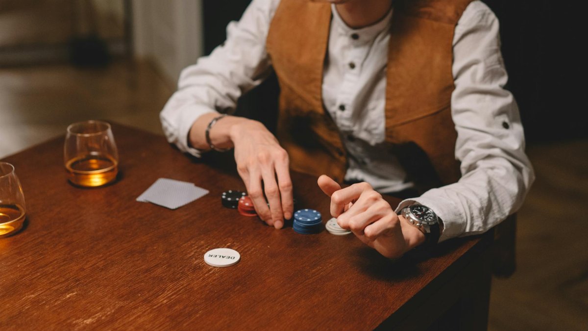 A man playing poker indoors, with poker chips and whiskey on a wooden table.