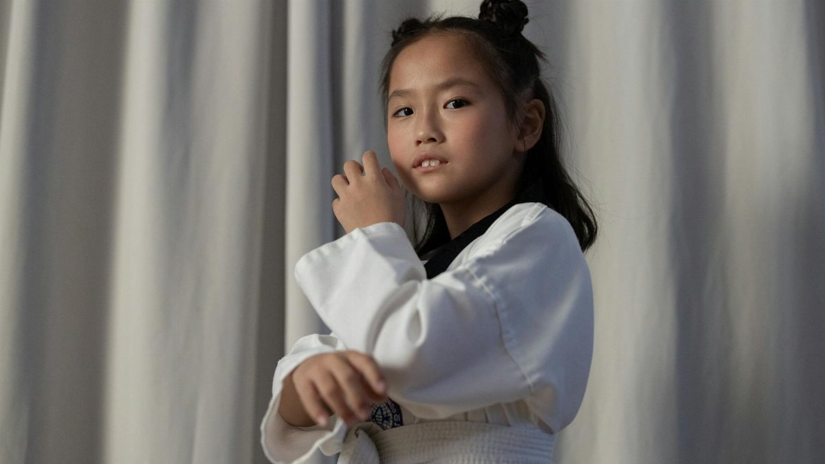 Confident young girl in a taekwondo uniform posing indoors.