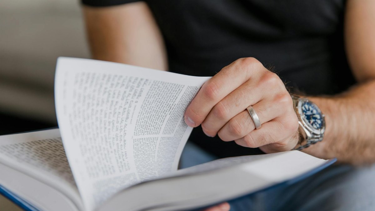 A close-up shot of a hand with a ring turning pages in an open book.